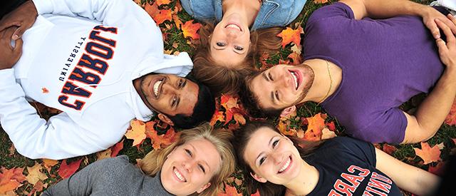 students in leaves smiling up at camera